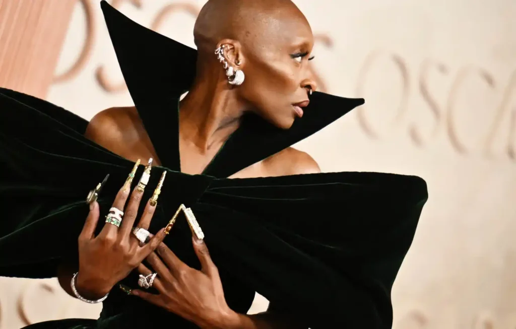 A striking figure showcasing a dramatic black gown with oversized shoulders, adorned with intricate rings and long, embellished nails.