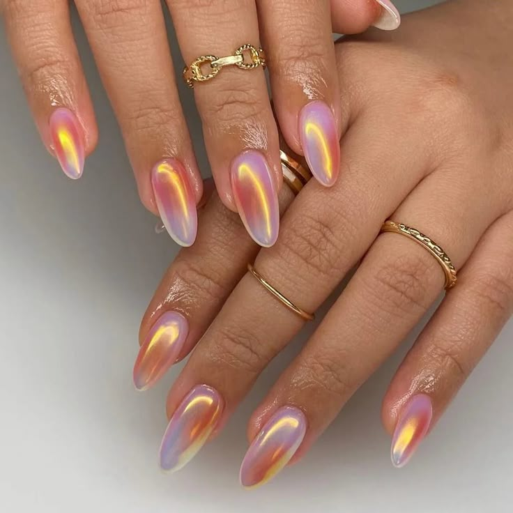 5 Chrome Nail Art Designs You Have to Try This Season 2 Beautifully manicured hands showcasing iridescent nails in shades of pink, orange, and purple, adorned with delicate gold rings.