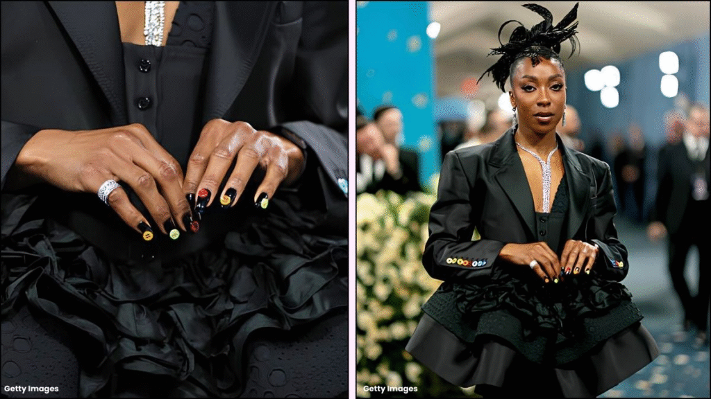A stylish individual showcases a black outfit with intricate ruffle details, displaying colorful nail art on both hands, complemented by striking jewelry and a bold hairstyle.