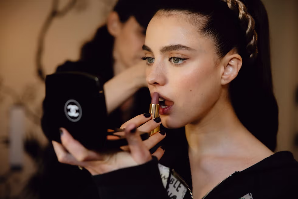 A woman applies lipstick while looking in a mirror, showcasing a focused makeup moment.